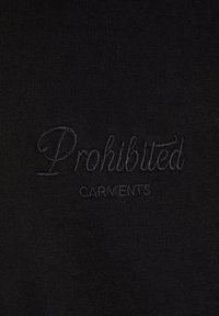 Svart stoff med hevet broderi av "Forbudte plagg" i kursiv skrift, sentrert på overflaten. Glatt tekstur.