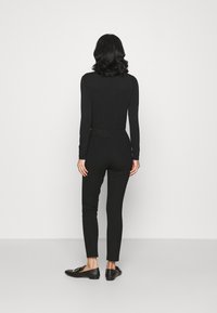 Černý top s dlouhým rukávem a přiléhavými kalhotami. Hladká tkanina, slim fit, minimalistický design. Černé mokasíny se zlatými kovovými akcenty.