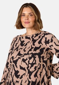 Maglietta a maniche lunghe beige con stampa astratta nera, dotata di scollatura rotonda e vestibilità comoda, realizzata in un tessuto leggero e morbido.