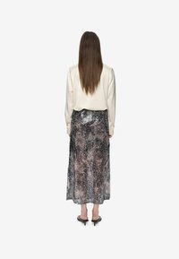 Blouse blanche à manches longues associée à une jupe semi-transparente en sequins noirs et argentés, atteignant la longueur du mollet. Sandales à talons noires.