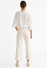 Hvid, løsthængende bluse med rullede ærmer, parret med lyse beige, højhalset, lige ben jeans og beige sneakers med grønne accenter.