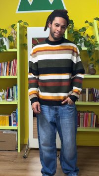 Pull rayé multicolore avec des motifs horizontaux en vert, orange, marron et blanc ; associé à un jean bleu clair ample.