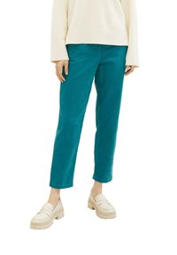 Pantalon en velours côtelé teal avec une coupe droite, associé à des mocassins beiges épais. Tissu texturé et coupe décontractée.