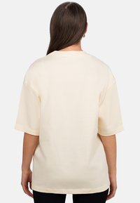 T-shirt oversized color crema realizzata in morbido cotone, con maniche corte e colletto rotondo, caratterizzata da una texture liscia e cuciture minimali.