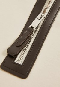 Fermoar din piele maro cu dinți metalici argintii și un tab de prindere elegant, având cusături contrastante pe margini.