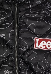 Giacca trapuntata nera con motivo ondulato bianco, zip silver e patch rosso con il logo "Lee" sulla zona del petto.