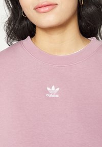 Rosa sweatshirt med rund halsringning och ribbade muddar, med en liten vit Adidas-logotyp på bröstet. Mjukt bomullsmaterial.