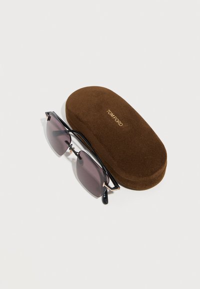Black-framed rimless sunglasses with dark lenses next to a brown velvet Tom Ford branded hard case on a white surface.