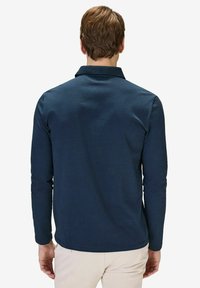 Mörkblå långärmad polo med textilstruktur, nedfällbar krage och stickad fåll. Har rak skärning och avslappnad passform.