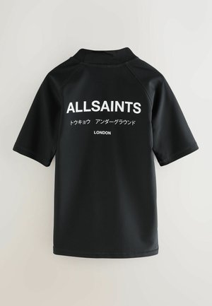 Schwarzer Rashguard mit kurzen Ärmeln aus weichem, elastischem Material. Auf der Rückseite befindet sich weißer Text mit den Worten "ALLSAINTS" und "LONDON."
