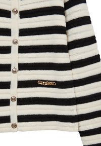 Cardigan a righe nero e crema con texture a coste, dotato di bottoni metallici e un dettaglio logo dorato vicino all'orlo.