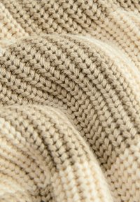 Nahaufnahme von weichem, strukturiertem beigen und cremfarbenem Strickmaterial mit dicker, grober Wolle und sichtbaren Maschenmustern.
