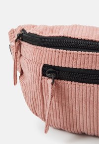 Borsa in corduroy rosa con superficie testurizzata, caratterizzata da una cerniera e particolari neri. Forma arrotondata con una piccola tasca laterale.