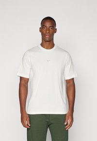 Hvid bomulds t-shirt med rund halsudskæring og korte ærmer, med et subtilt gråt logo centreret på brystet. Glat tekstur.