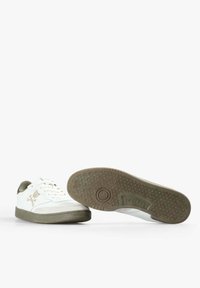 Zapatillas blancas de caña baja con suelas, cordones y logotipo verde oliva en el lado, un zapato mostrando la suela estampada con la marca "Scalpers".