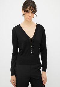 Maglione nero a maglia con scollatura a V, maniche lunghe e una fila di bottoni decorativi sul davanti. Tessuto morbido e strutturato con leggero luccichio.
