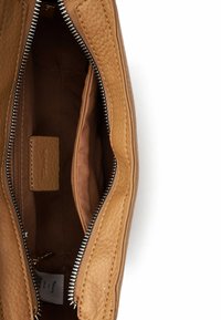 Ādas soma tan krāsā iekšpuse ar centrālu rāvējslēdzēja nodalījumu, gludu tekstūru un vienu plakanu kabatu. Rāvējslēdzēja detaļas redzamas gar malām.