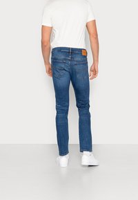 Vaqueros de mezclilla en azul oscuro con un ajuste slim. Presentan dos bolsillos traseros, costuras en contraste y un parche de cuero marrón en la cinturilla.