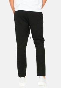Pantaloni da jogging neri con una vestibilità slim, caratterizzati da una vita elasticizzata e cordoncino, realizzati in tessuto morbido. Abbinati a sneaker bianche.
