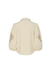 Cremefarvet bluse med voluminøse pufærmer, der har intrikate brune broderier på manchetterne, kravehalset og en lige skæring i kanten.