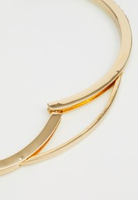 Gouden metalen collier met gebogen segmenten, een gladde textuur en een centrale opening. Gepolijste afwerking, minimalistisch ontwerp.