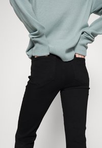 Jean en denim noir avec poches et coupe slim, associés à un pull en maille bleu clair avec des poignets et un ourlet côtelés.