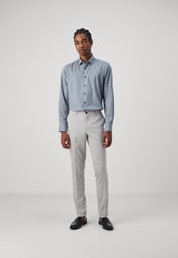 Blaue gemusterte langärmelige Bluse mit Knöpfen, kombiniert mit hellgrauen, maßgeschneiderten Hosen und schwarzen Mokassins. Schlichtes, modernes Design.