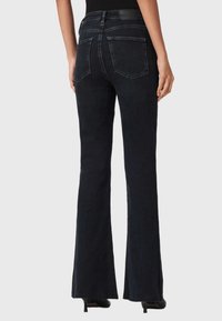 Tumman denim-materiaalin leveälahkeiset farkut, joissa on takataskut, pieni kuluminen ja musta nahkalaatta vyötäröllä. Farkut ovat tiukat reidestä ja levenevät lahkeista.