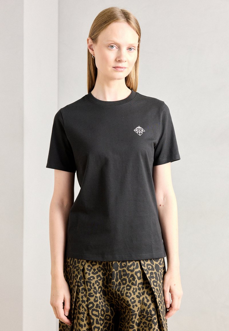 T-shirt in cotone nero con maniche corte e scollatura rotonda, caratterizzato da un piccolo logo bianco sul petto. Indossato con una gonna a stampa leopardata.