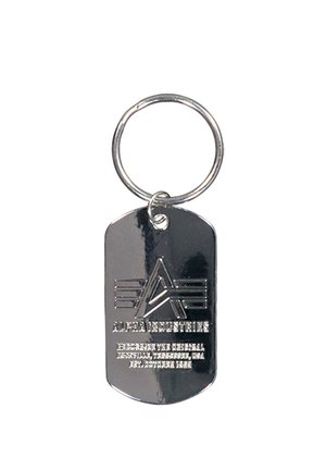 Metall-Schlüsselanhänger mit einem Ring, der ein geprägtes Logo eines stilisierten "A" und darunter den Text "ALPHA INDUSTRIES" zeigt.