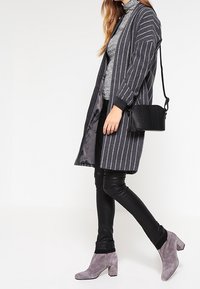 Cardigan lungo grigio a righe con bordi neri sopra un dolcevita grigio, abbinato a pantaloni in pelle neri e stivaletti grigi. Borsa a tracolla nera.