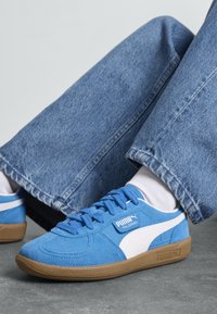 Blauwe sued sneakers met witte accenten en een bruine rubberen zool. Kenmerkt platte veters, een ronde neus en een logo aan de zijkant.