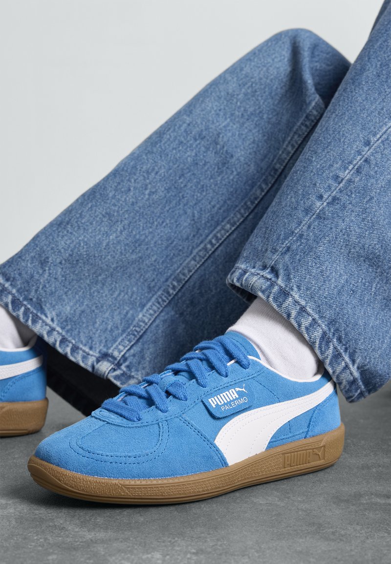 Blauwe sued sneakers met witte accenten en een bruine rubberen zool. Kenmerkt platte veters, een ronde neus en een logo aan de zijkant.