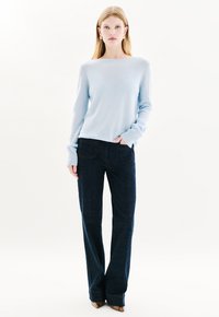 Lichtblauwe gebreide trui met lange mouwen, gecombineerd met donkerblauwe flare jeans. Opvallende details zijn de casual pasvorm en de gekartelde stof.