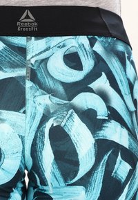 Legginsy Reebok CrossFit mają czarny pas i abstrakcyjny wzór w kolorze turkusowym i granatowym, wykonane z elastycznej tkaniny o gładkiej fakturze.