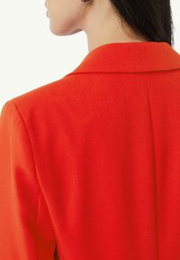 Bright red blazer with a notched collar, featuring a smooth texture and tailored fit, showing stitching and a single rear vent detail.