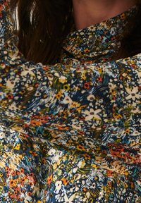Donna che indossa un top a maniche lunghe con fantasia floreale multicolore, con i capelli scuri parzialmente visibili.