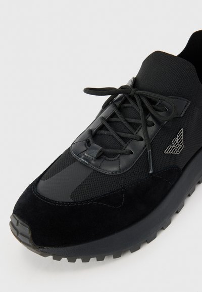 Black athletic shoe featuring a combination of mesh and suede materials, with a textured rubber sole and prominent logo detail.