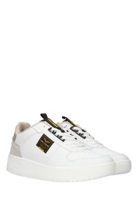 Baskets en cuir blanc avec des accents beige et noir, présentant une surface texturée, des lacets noirs et une étiquette logo sur le côté.