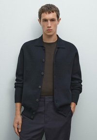 Dark navy knit cardigan with a collared neckline, button closures, and ribbed cuffs, layered over a brown short-sleeve shirt.