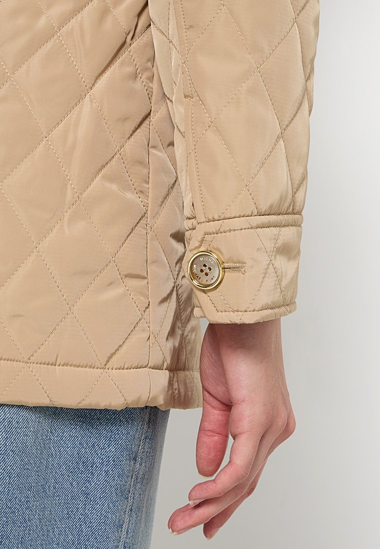 Manica di giacca trapuntata beige con dettagli in bottone dorato. Tessuto liscia con una leggera lucentezza. Design polsino, vestibilità su misura e linee pulite.