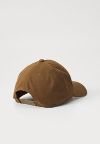 Brown cotton baseball cap with a curved peak, adjustable strap, and a textured fabric. Features a logo on the back strap.