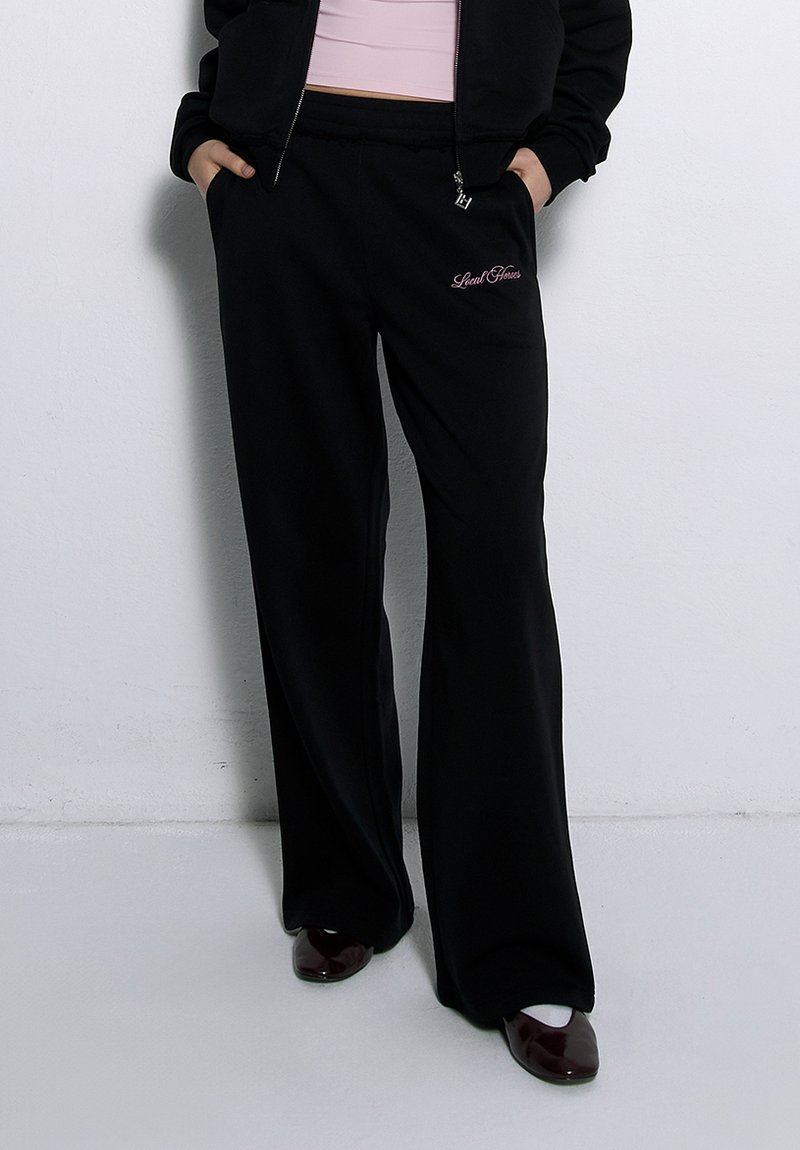 Schwarze Sweatpants mit weitem Bein-Design, aus einem weichen Stoff gefertigt, mit einem bestickten rosa Logo und seitlichen Taschen.