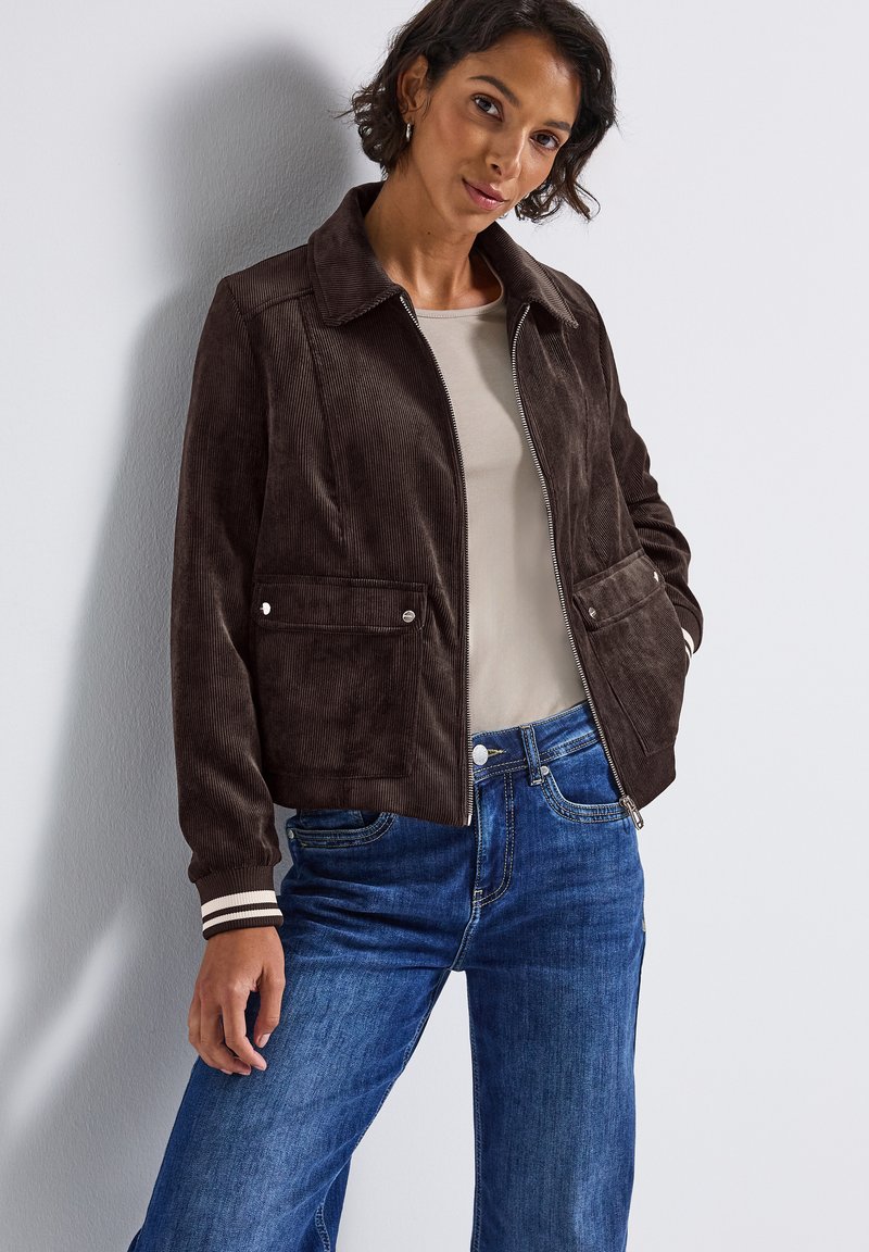 Brun kordflodjacka med krage, främre dragkedja, två fickor med lock och randiga muddar, kombinerad med blå denimjeans.