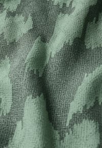 Kangas, jossa on vihreä ja tummanharmaa abstrakti kuvio, jossa on teksturoitu kudonta. Suunnittelussa on epäsäännöllisiä, siveltimenvedontyylisiä muotoja.
