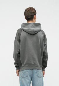 Gray hooded sweatshirt with a relaxed fit, ribbed cuffs and hem, featuring a smooth texture and contrasting seam details. Worn with light blue jeans.