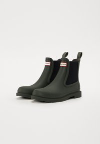 Bottes Chelsea en caoutchouc vert avec panneaux élastiques noirs sur les côtés, hauteur de cheville sculptée et semelle texturée pour une meilleure adhérence. Équipées de languettes pour un enfilage facile.