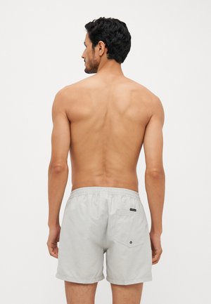 Shorts en coton gris clair avec une taille élastique et une poche arrière unique, ornés d'une petite étiquette. La surface semble lisse.
