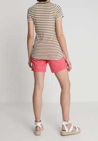 Camisa de manga corta a rayas en beige y marrón, combinada con pantalones cortos rosas y sandalias blancas. La camisa tiene un escote redondeado y un ajuste Slim.