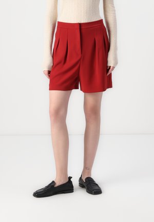 Røde, plisserte shorts med en skreddersydd midje, laget av et glatt stoff. Kombinert med svarte lær slip-on sko.